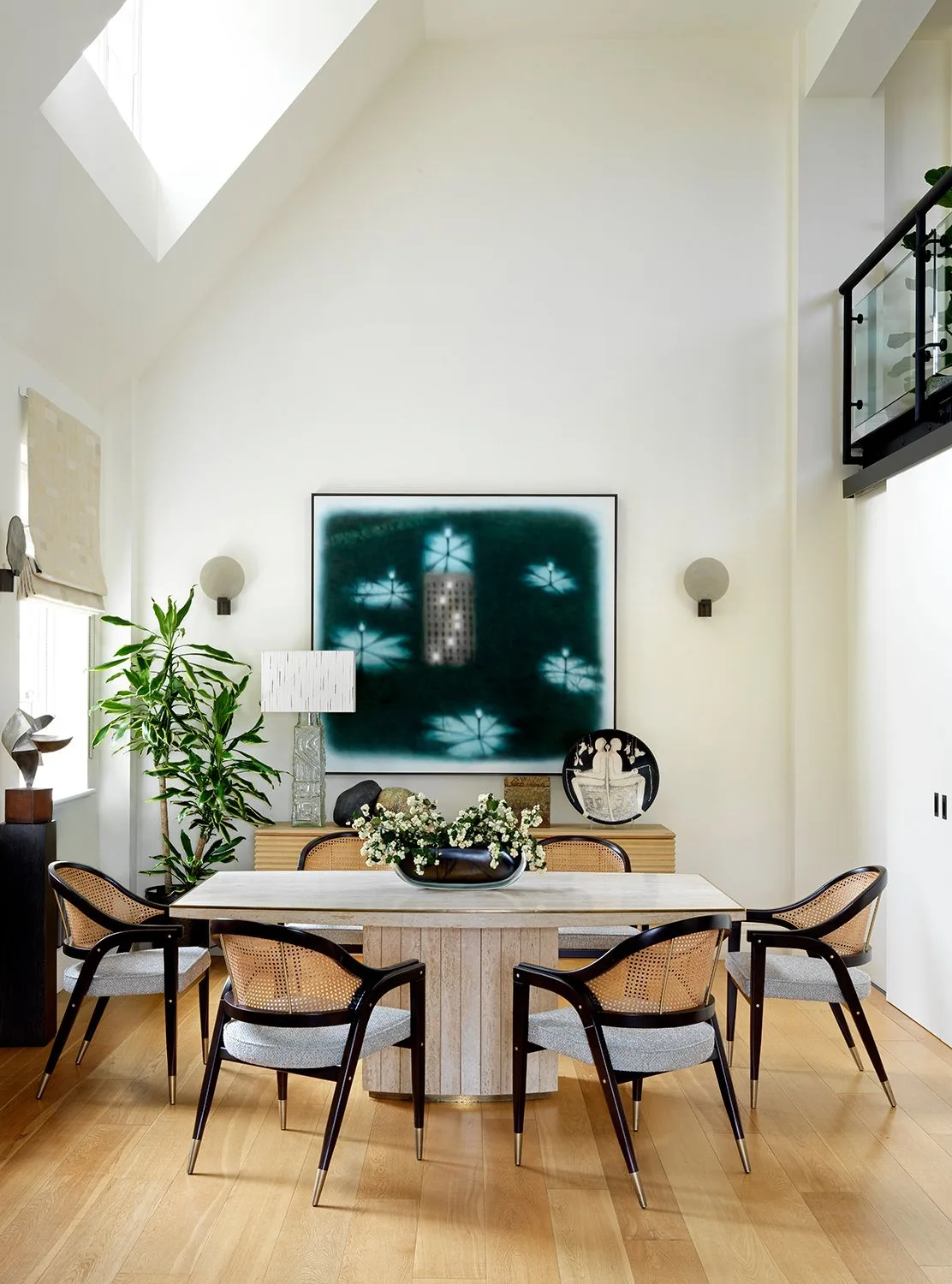 Pale wood ribbed sideboard beneath teal artwork behind a pale dining table and black woven chairs