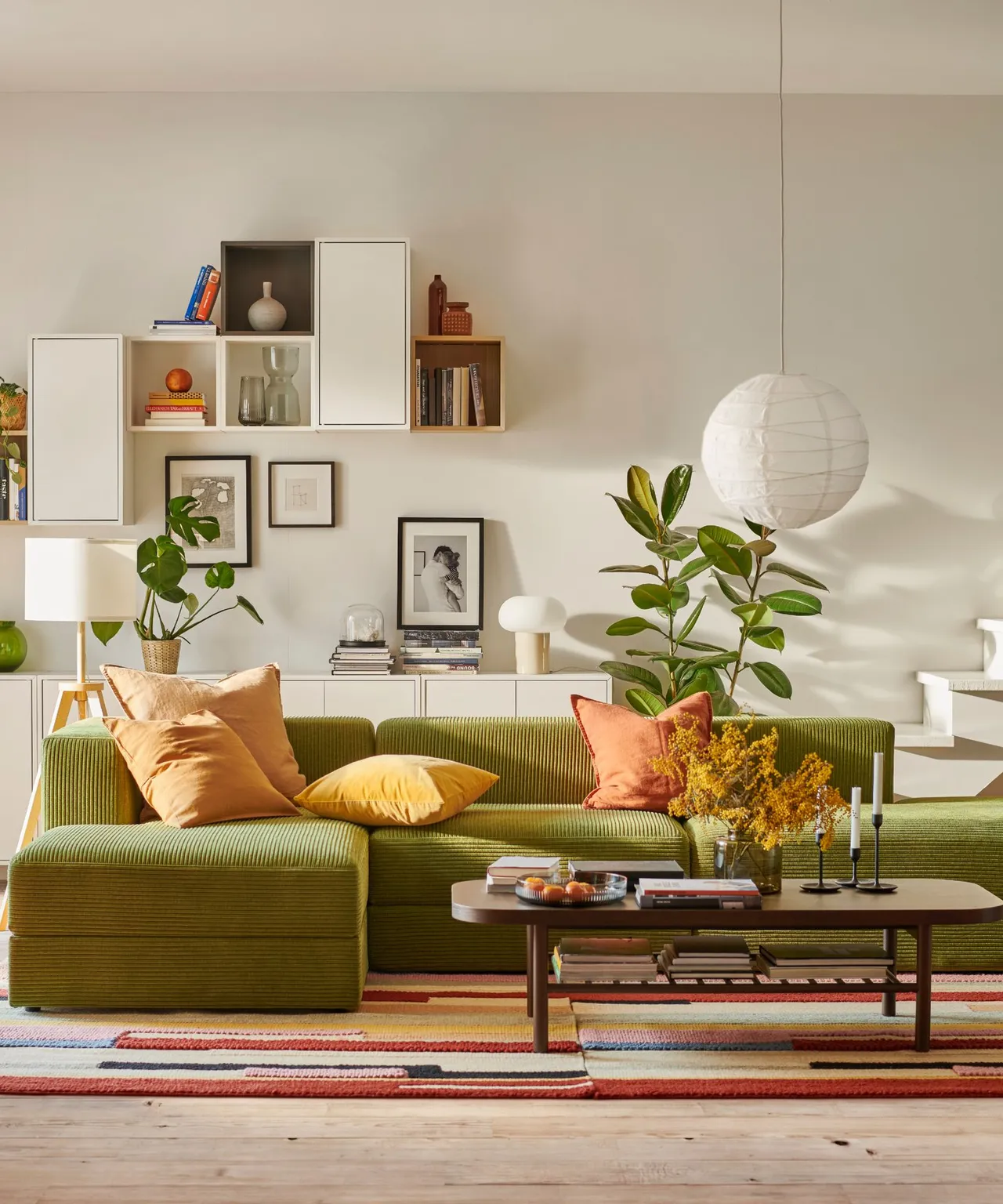 An olive-green sofa sits below open wall shelves with warm orange cushions.