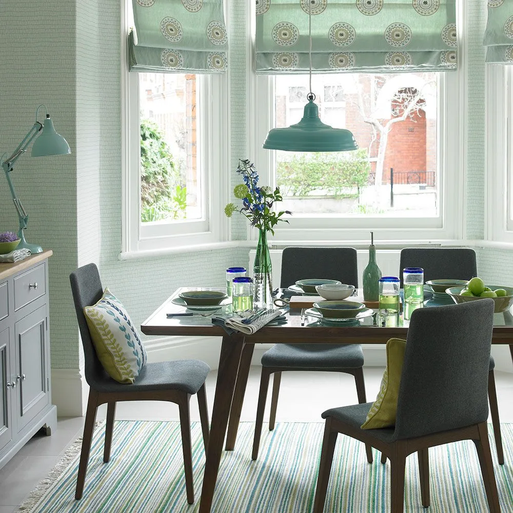 Green metal pendant above a dark dining table with gray chairs, patterned blinds and green walls
