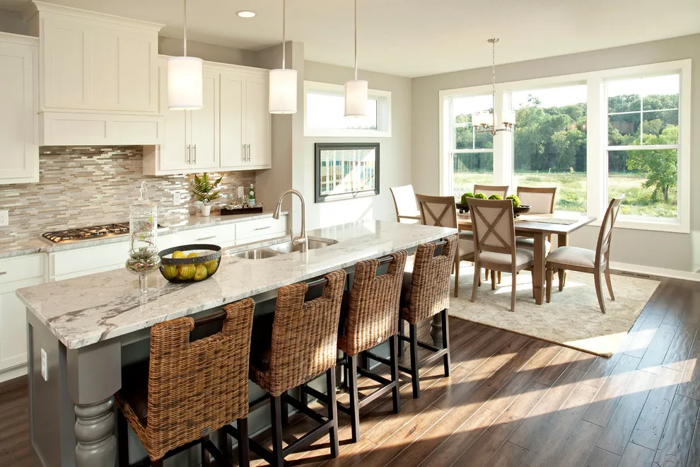 Woven stools line a pale kitchen island opposite cream cabinets and a patterned backsplash