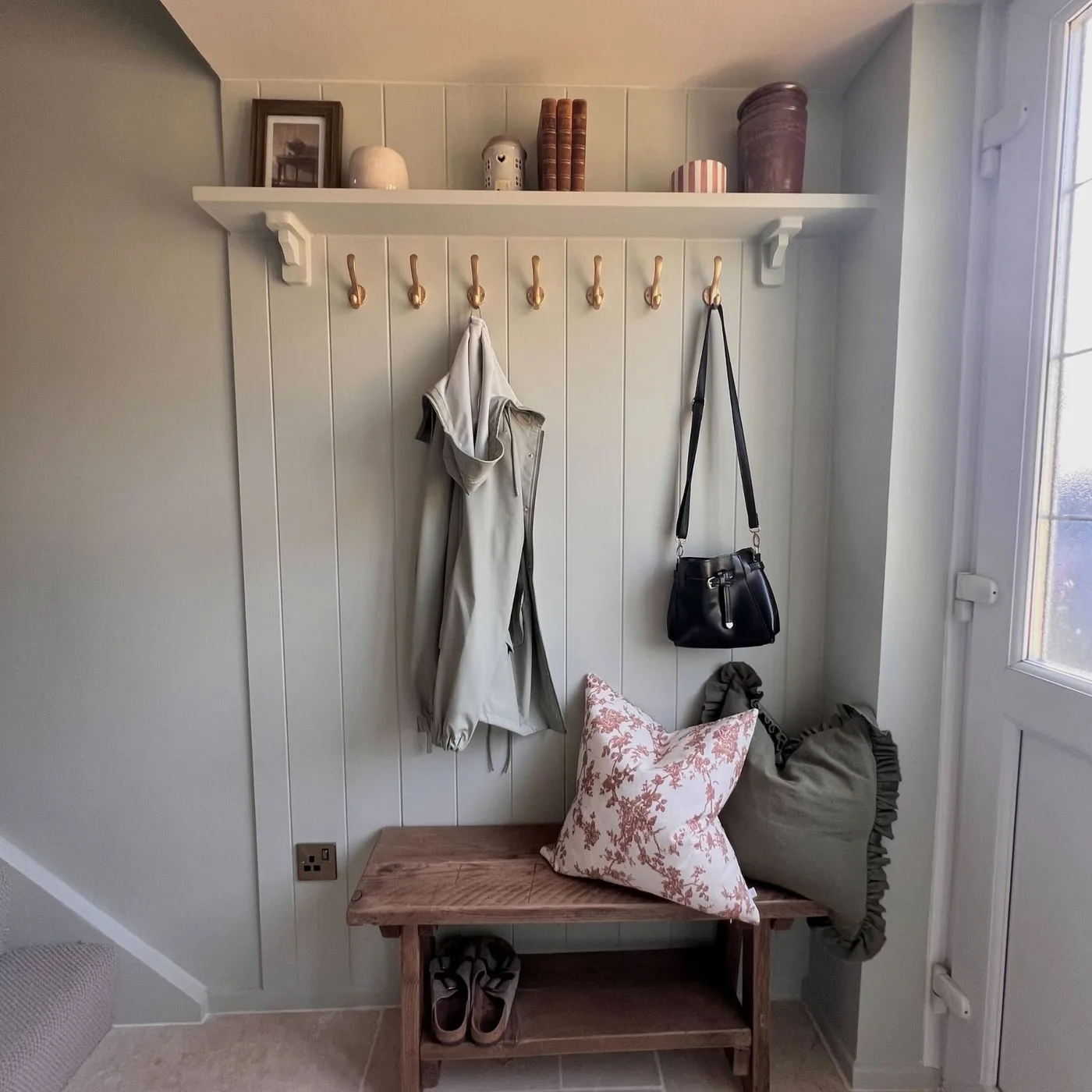 Compact gray paneled entry beside glazed white door with white shelf, hooks and wood bench