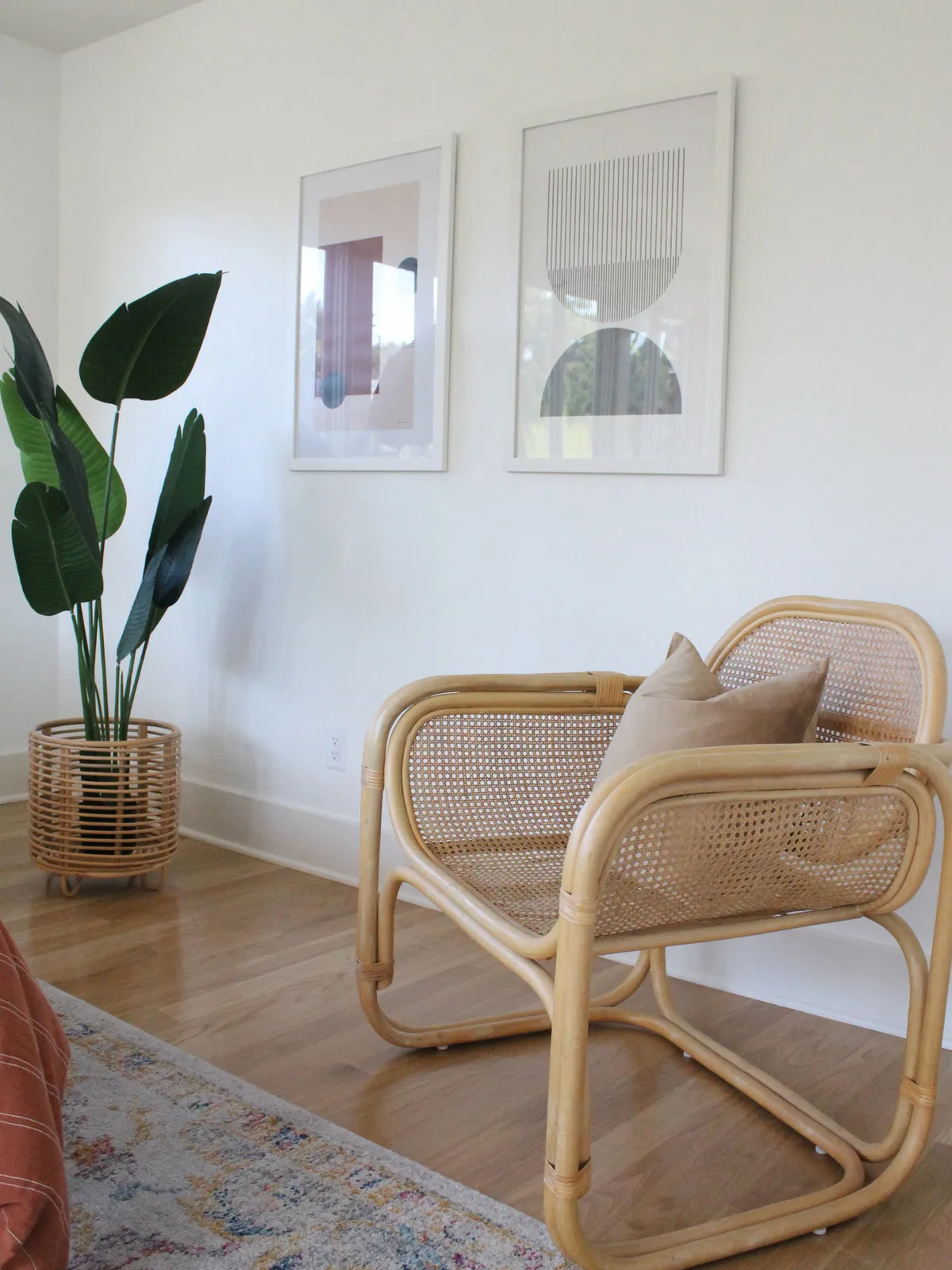 A pale rounded cane chair sits near a small timber table and light wall art.