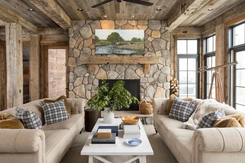 Rustic living room with stone fireplace, wood ceiling and beams, facing pale sofas, checked cushions and white coffee table