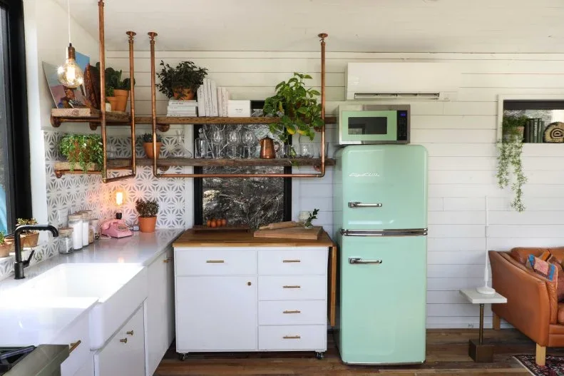 Compact white kitchen with copper-colored shelf supports, patterned backsplash, plants and a mint refrigerator.