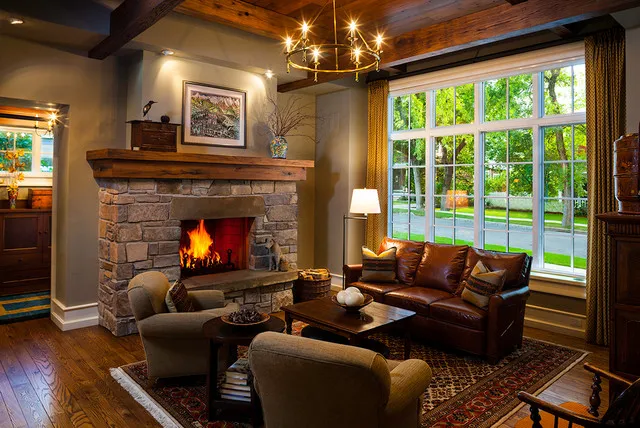 Dark seating sits around a stone fireplace beneath timber beams, with a lamp near the window.