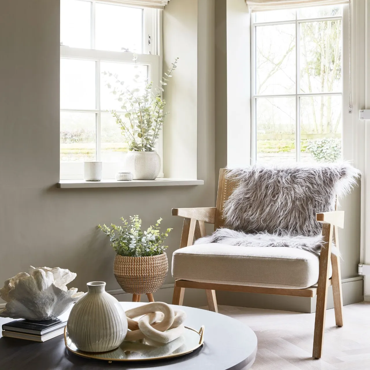 A pale timber armchair sits near a window with a soft textured throw across its back.