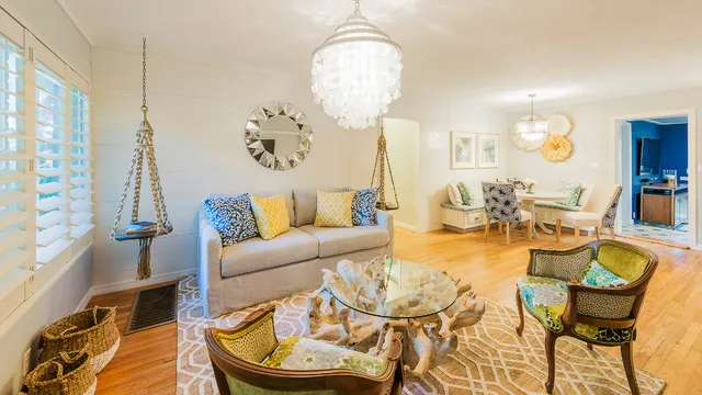 Pale seating sits with woven chairs, warm cushions and a light rug beneath broad windows.