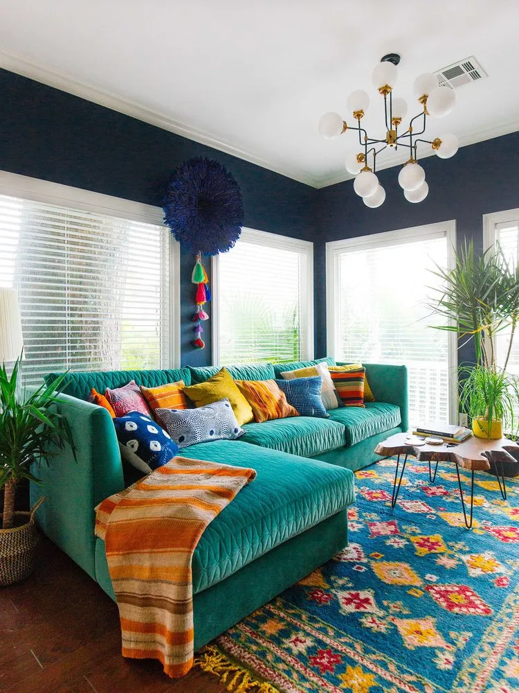 A vivid green sofa sits beneath dark upper walls with warm patterned cushions and a colorful rug.