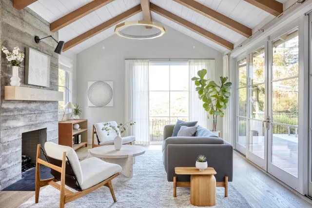 Exposed timber beams cross a pale room above restrained seating and a broad window.