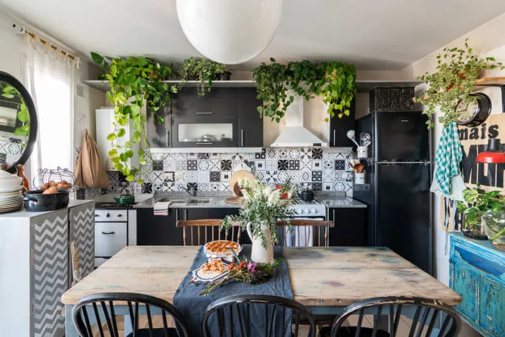 Black-and-white kitchen with trailing plants, patterned tiles, a wooden dining table and dark chairs.