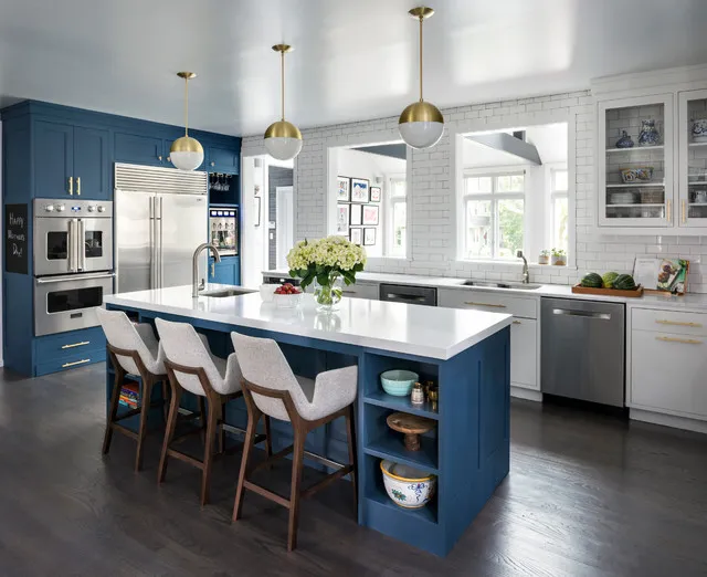 Navy cabinets and an island with open end shelves sit beside white counters and upper cupboards beneath three rounded warm-colored pendants