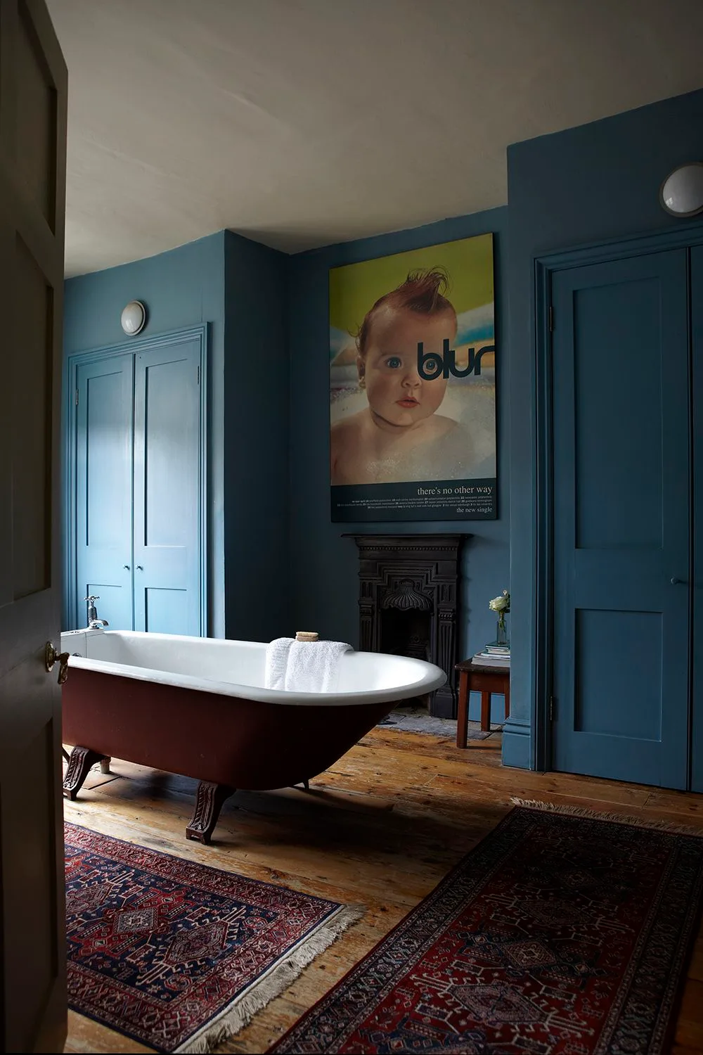 Deep blue paneled walls and doors surround a dark clawfoot bath beneath framed artwork