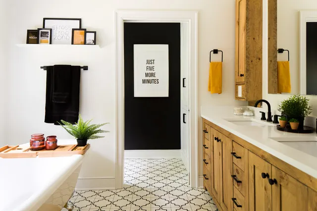 A timber vanity stands beside a pale bath over a small geometric floor pattern.