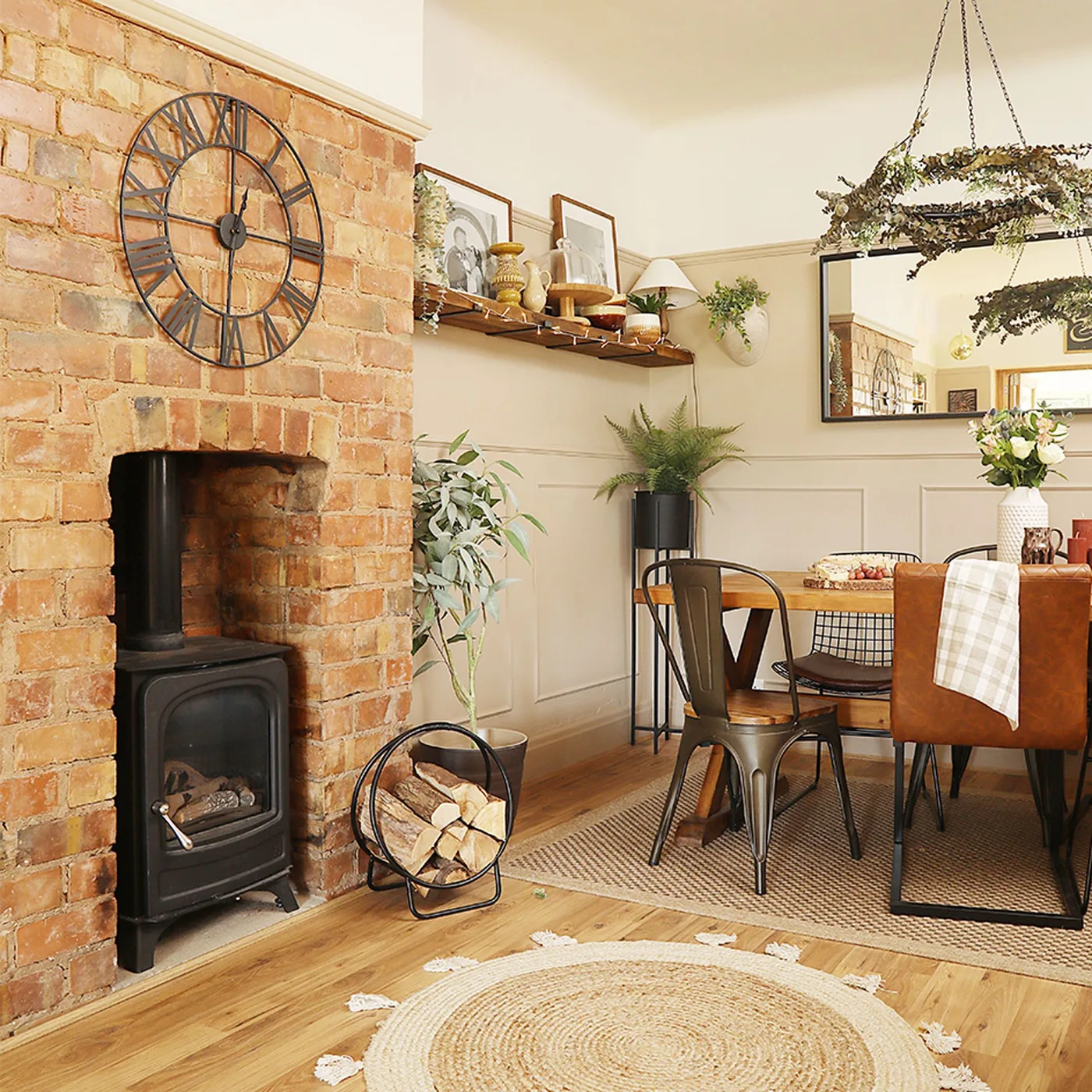 Dining room with a brick hearth, dark stove, wooden dining table, mixed chairs, woven rug and a hanging chandelier.
