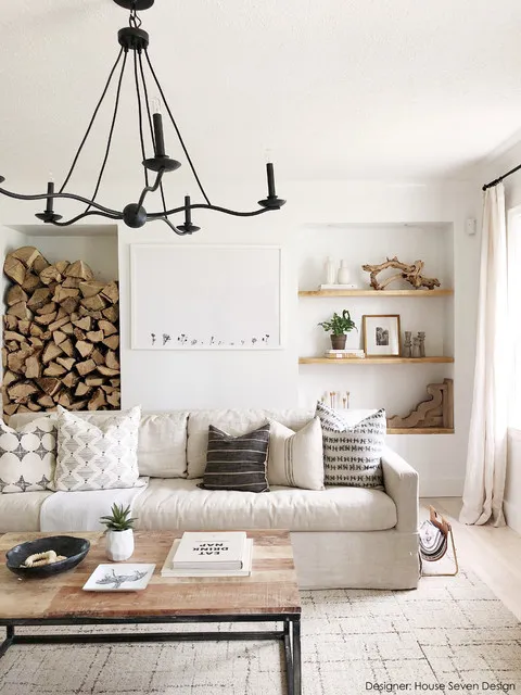 A pale sofa sits beside a modest timber coffee table and neatly stacked logs.