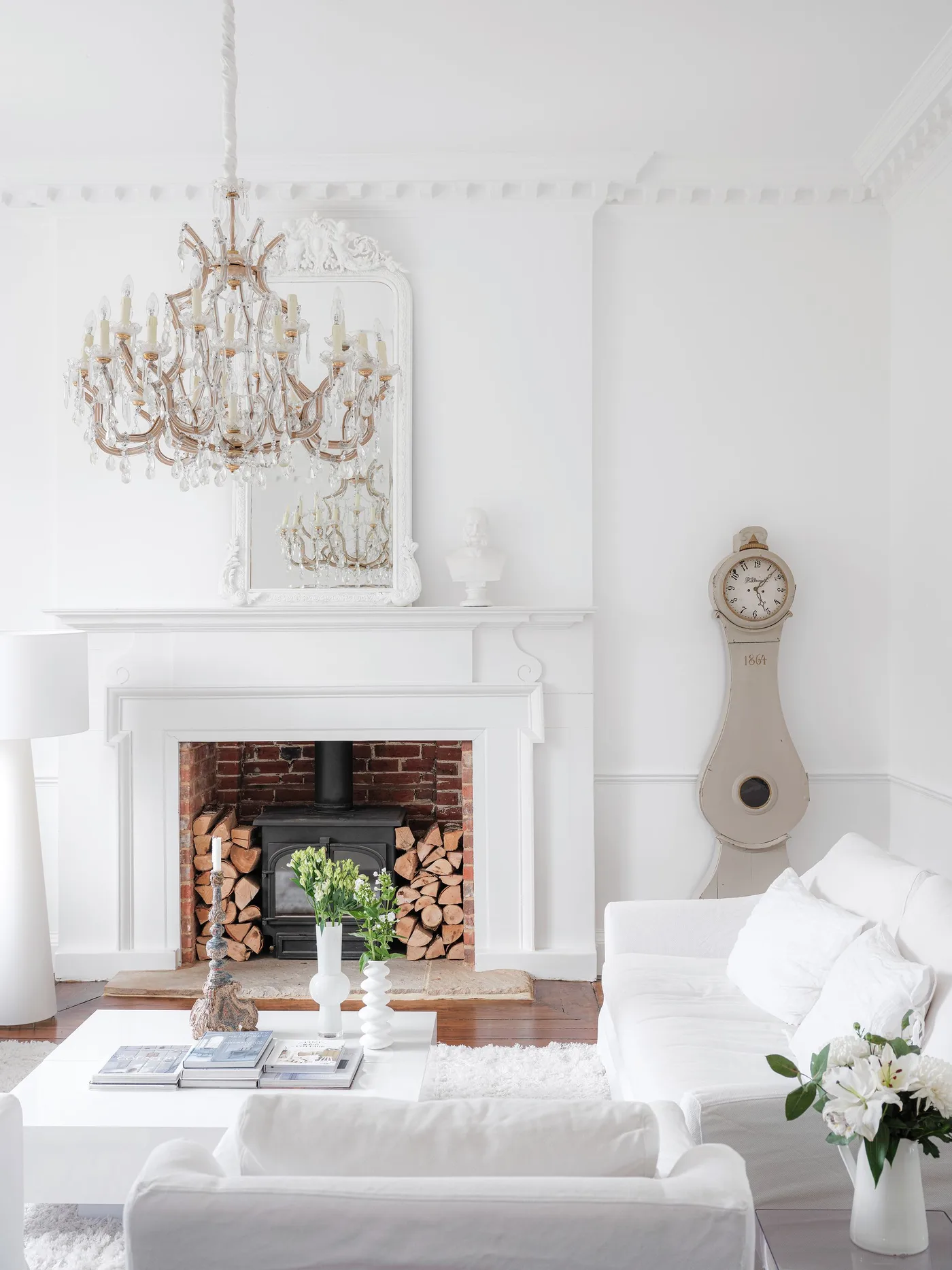 White ornate fireplace and mirror with red brick stove recess, pale clock and white seating