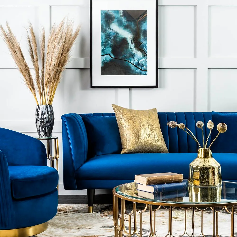 A vivid blue sofa sits against pale paneling beside warm metallic tables and a gold cushion.