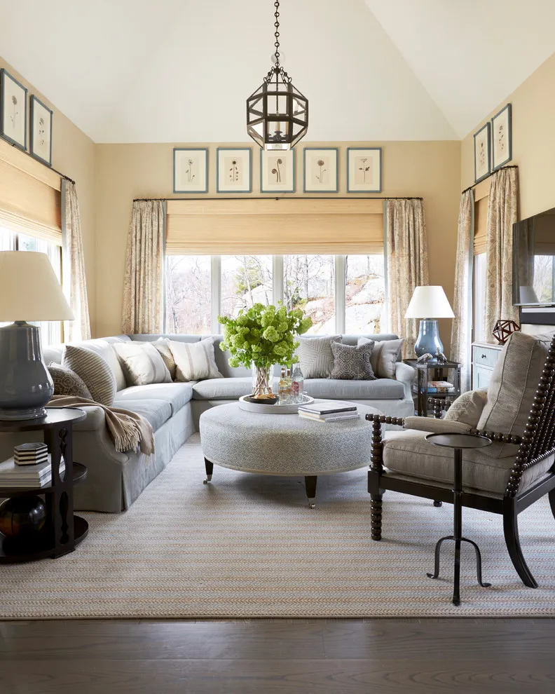 A dark spindle chair with pale cushions sits beside a blue-gray sectional and round ottoman