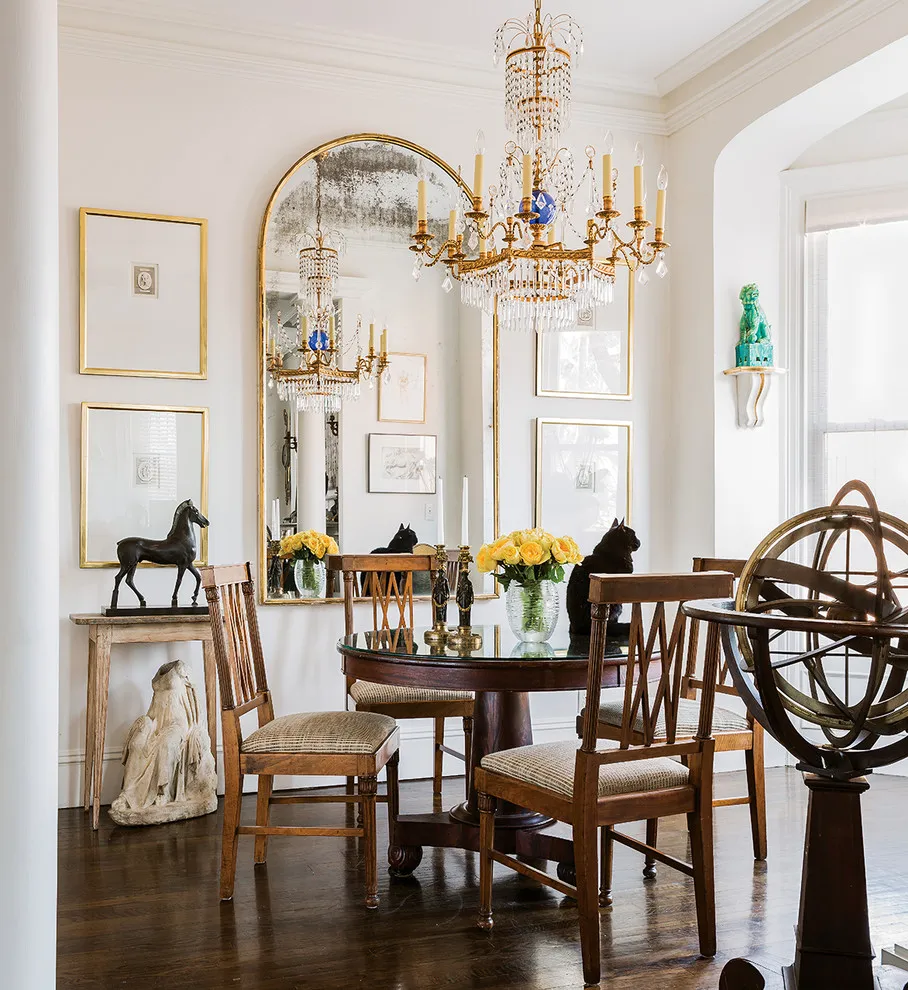 A round table sits beside timber chairs and a large mirror in a bright apartment
