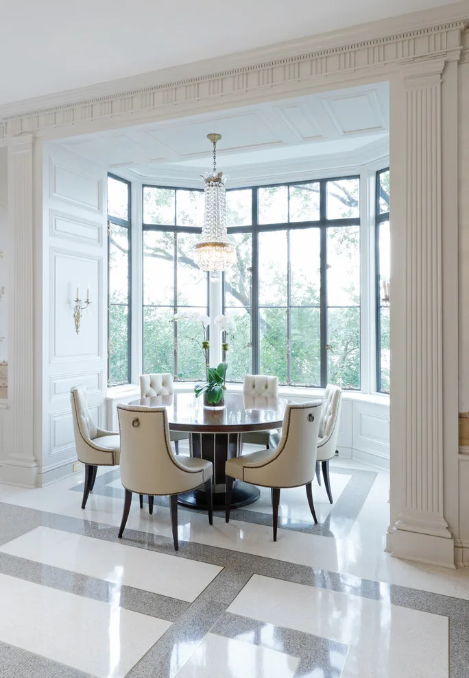 A small round table sits with pale chairs in a bright window bay