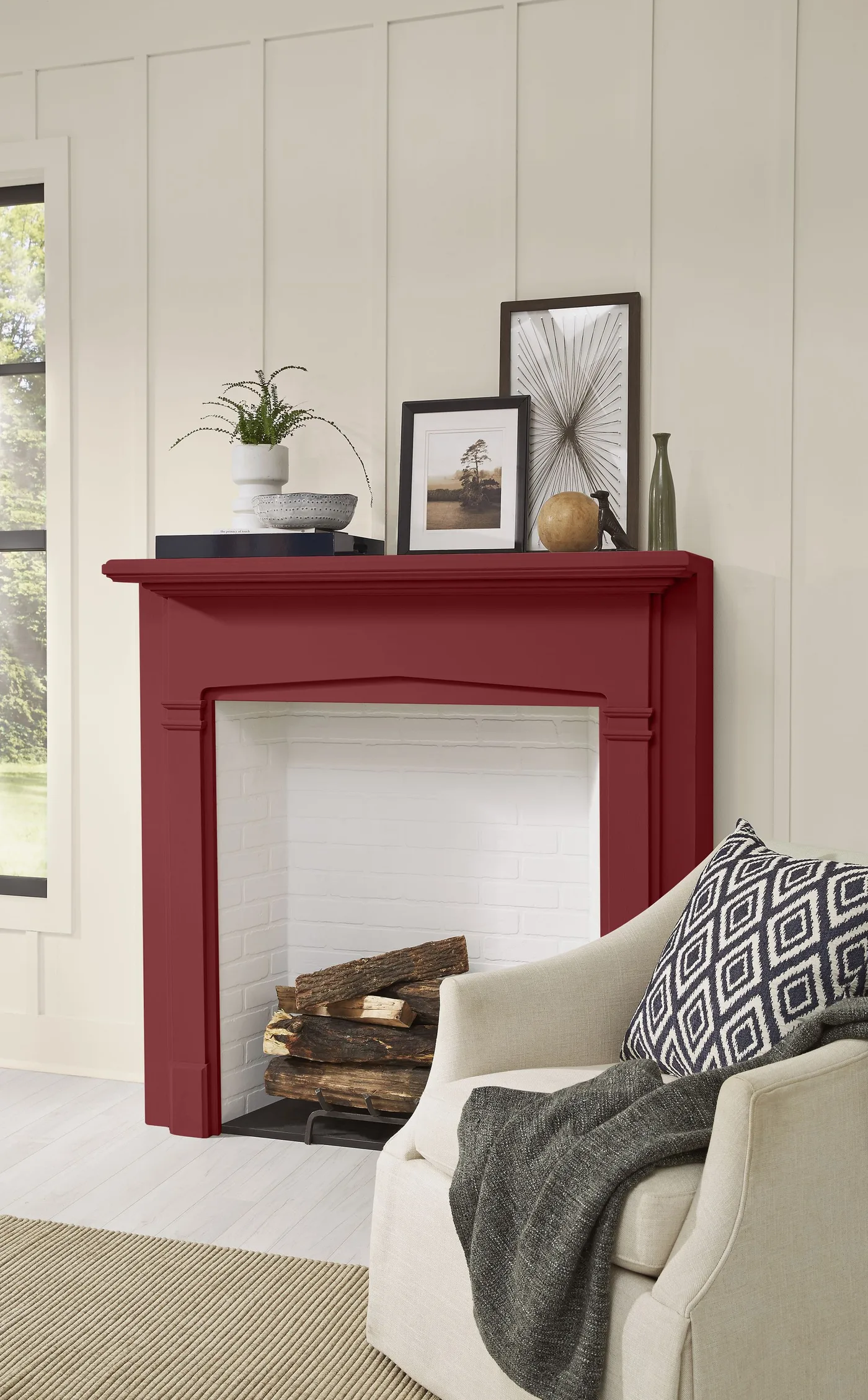 Deep red mantel with layered framed pictures, small plant, vessels and pale paneled wall