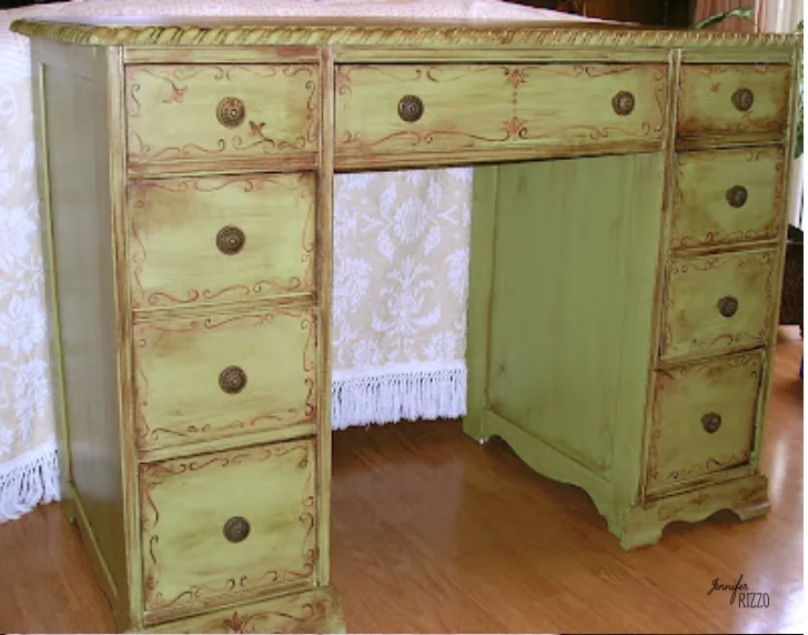 A pale green drawer desk with reddish decorative lines and small warm metal knobs stands before light curtains