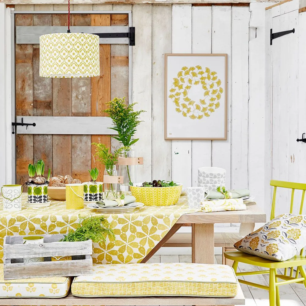 Yellow-green patterned drum pendant above a pale wood table in a white-paneled dining room