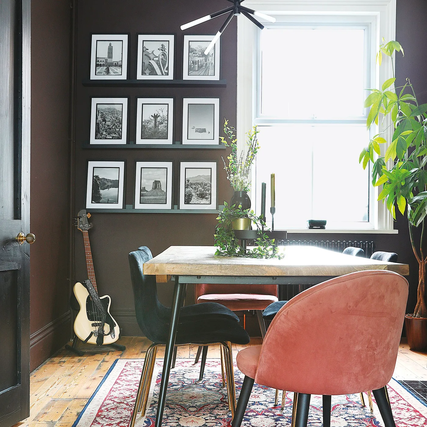 Three dark picture ledges with black and white framed photographs beside a dining table and pink chair