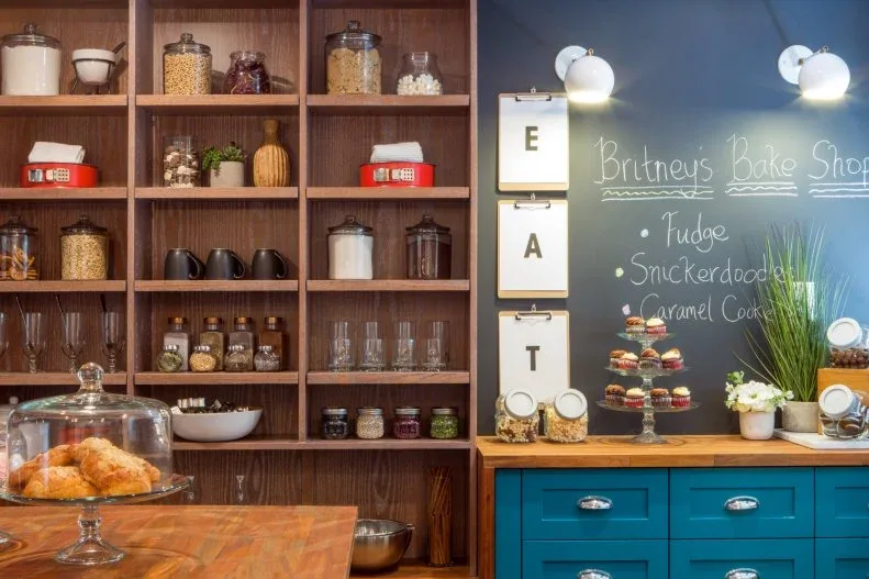 Wood pantry cubbies holding jars and cookware beside teal drawers, chalkboard and baking worktop
