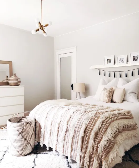 A pale bed sits beneath simple wall details with a softly patterned throw across its end.