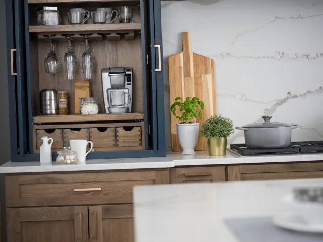 An open black-framed cupboard reveals timber shelves, mugs, drawers and coffee equipment above a pale counter.