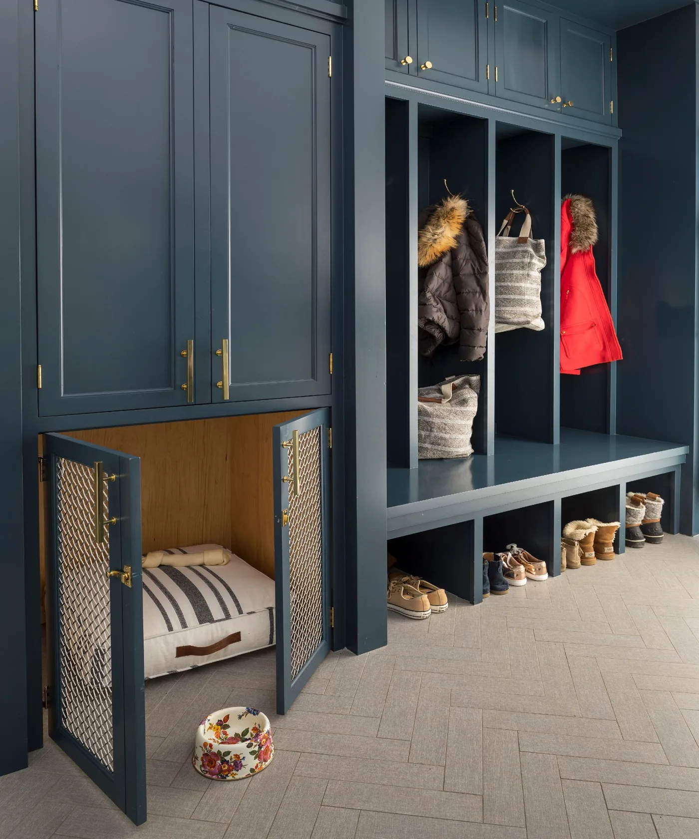 Navy mudroom with tall cupboards, divided hanging bays, open shoe spaces and a low wood-lined pet recess with mesh-front doors