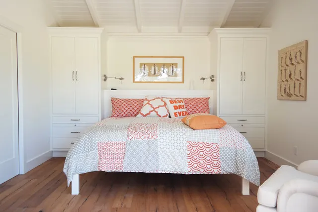 A pink-and-white quilt covers a bed against pale paneled walls.