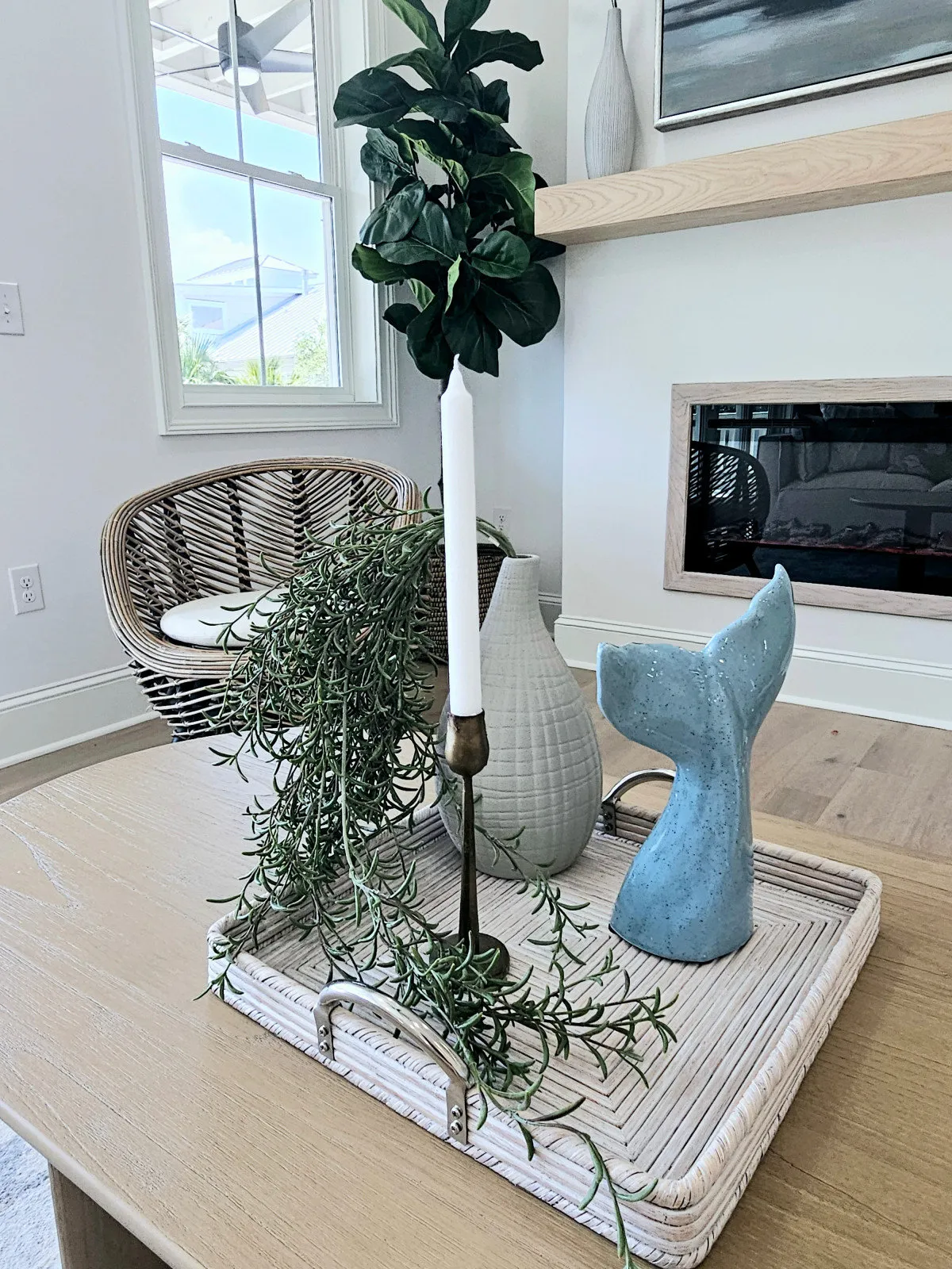 A pale table holds a small blue sculptural object beside a woven chair and light fireplace.