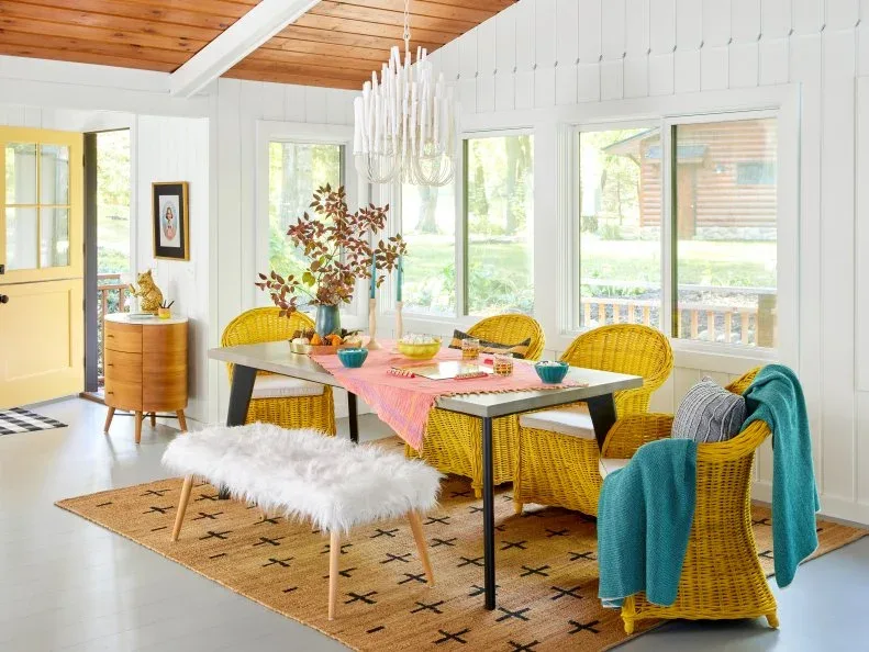 Pale dining room with yellow woven chairs, a rectangular table, a fluffy-covered bench, pink table runner and warm wood ceiling