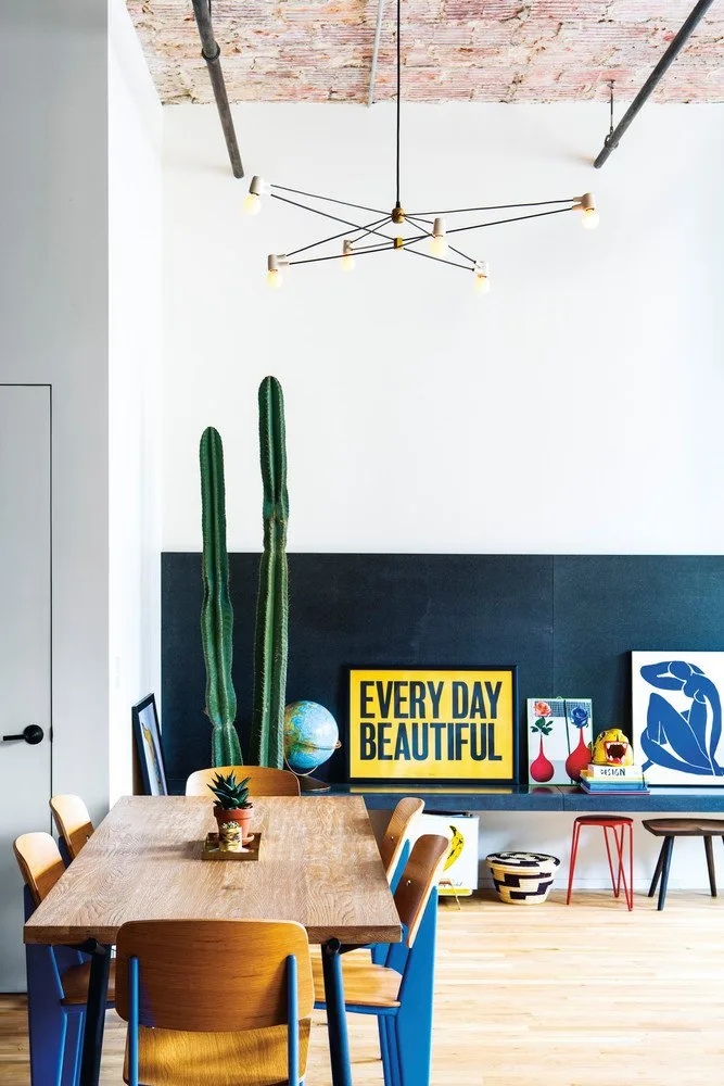 Leaning colorful prints and a globe against a dark lower dining wall beneath a tall pale upper wall