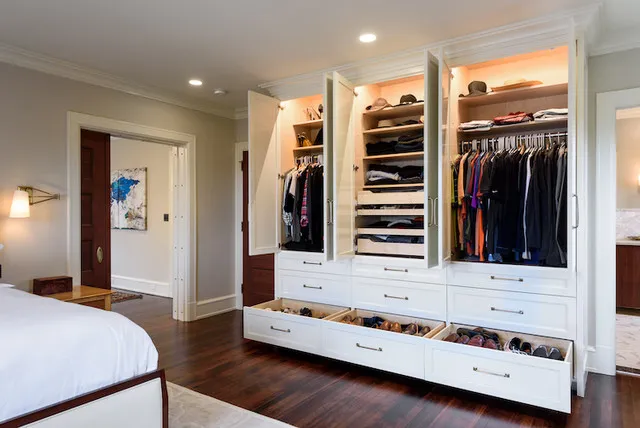 An open wardrobe displays hanging space, shelves and drawers beside a bed.