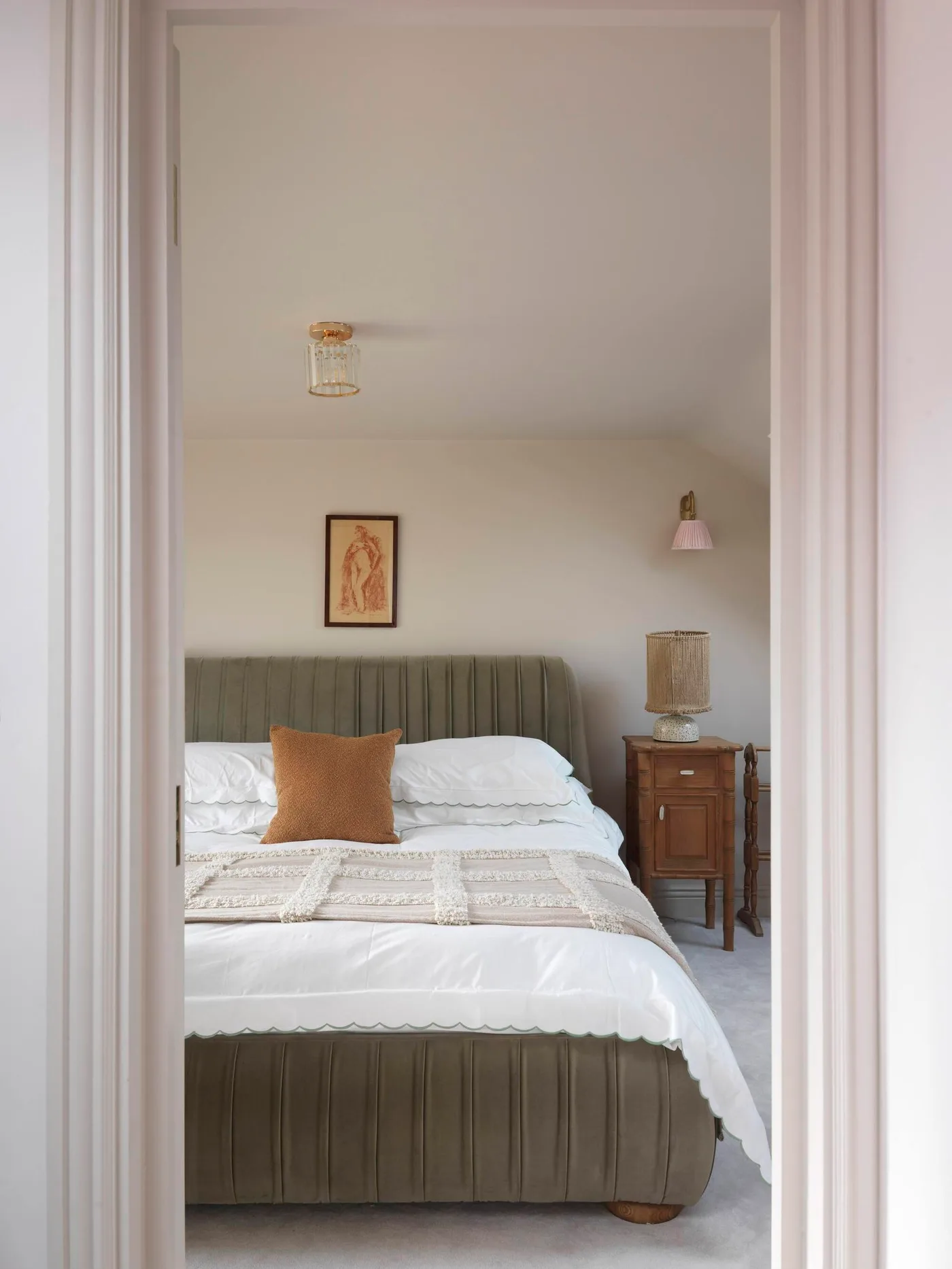 Muted green upholstered bed with pale bedding, an ochre cushion and a wood bedside cabinet