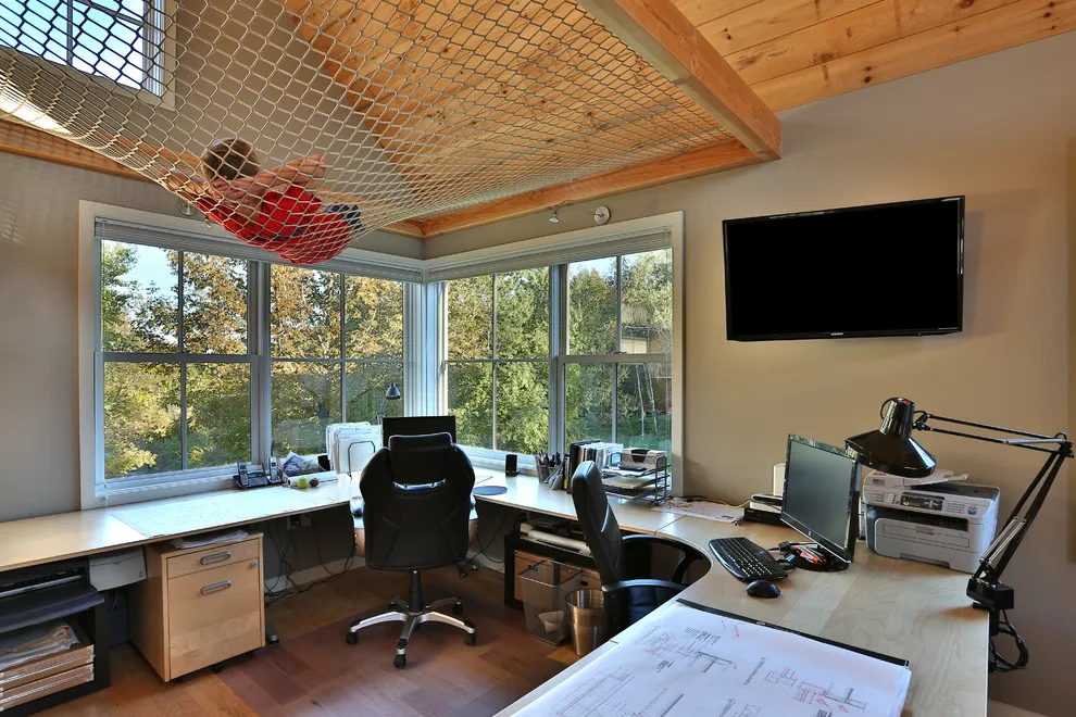 Desks sit beneath a timber ceiling beside broad windows in a studio