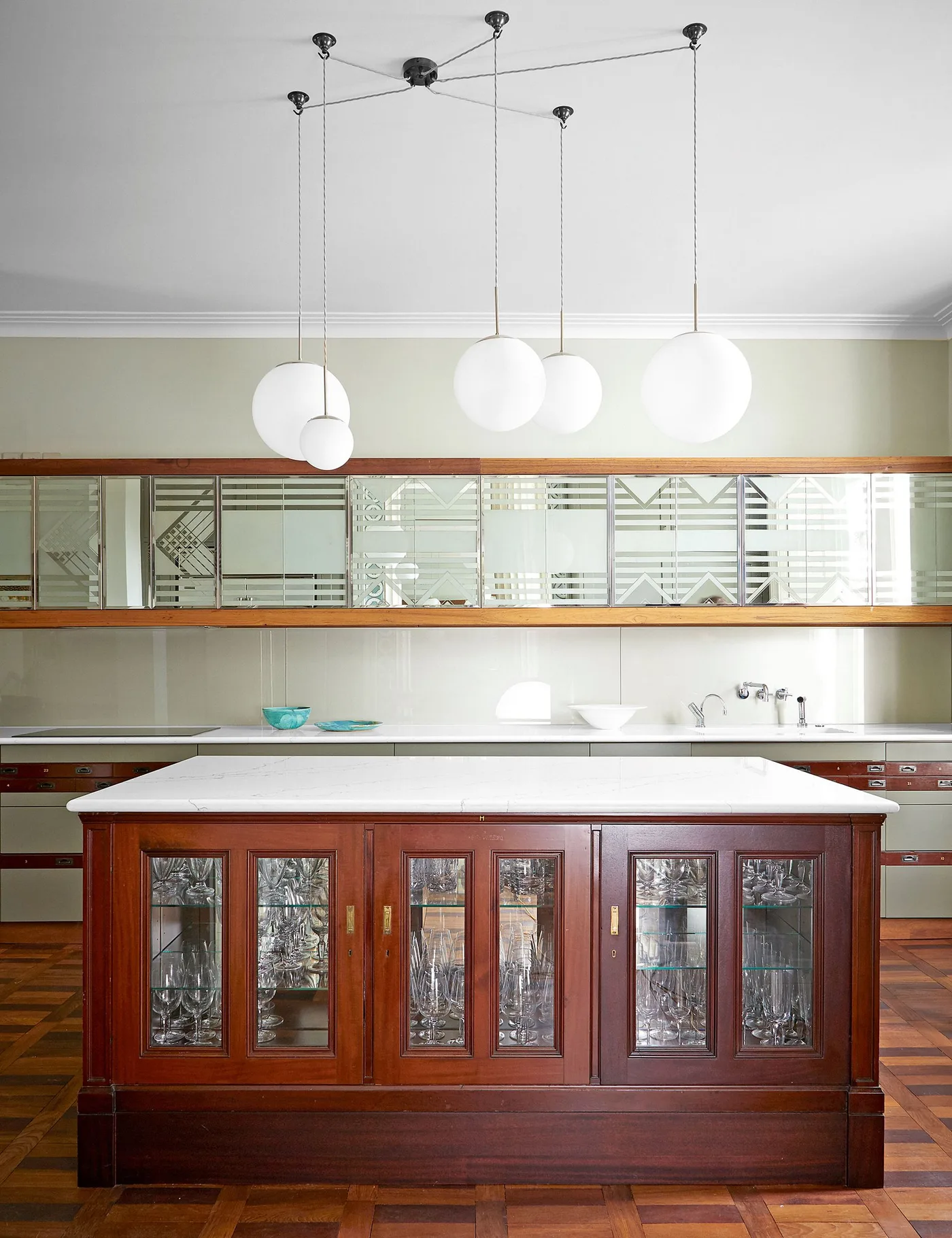 Reddish-brown kitchen island with glazed cabinet doors, a pale counter and a long decorative mirror above it.