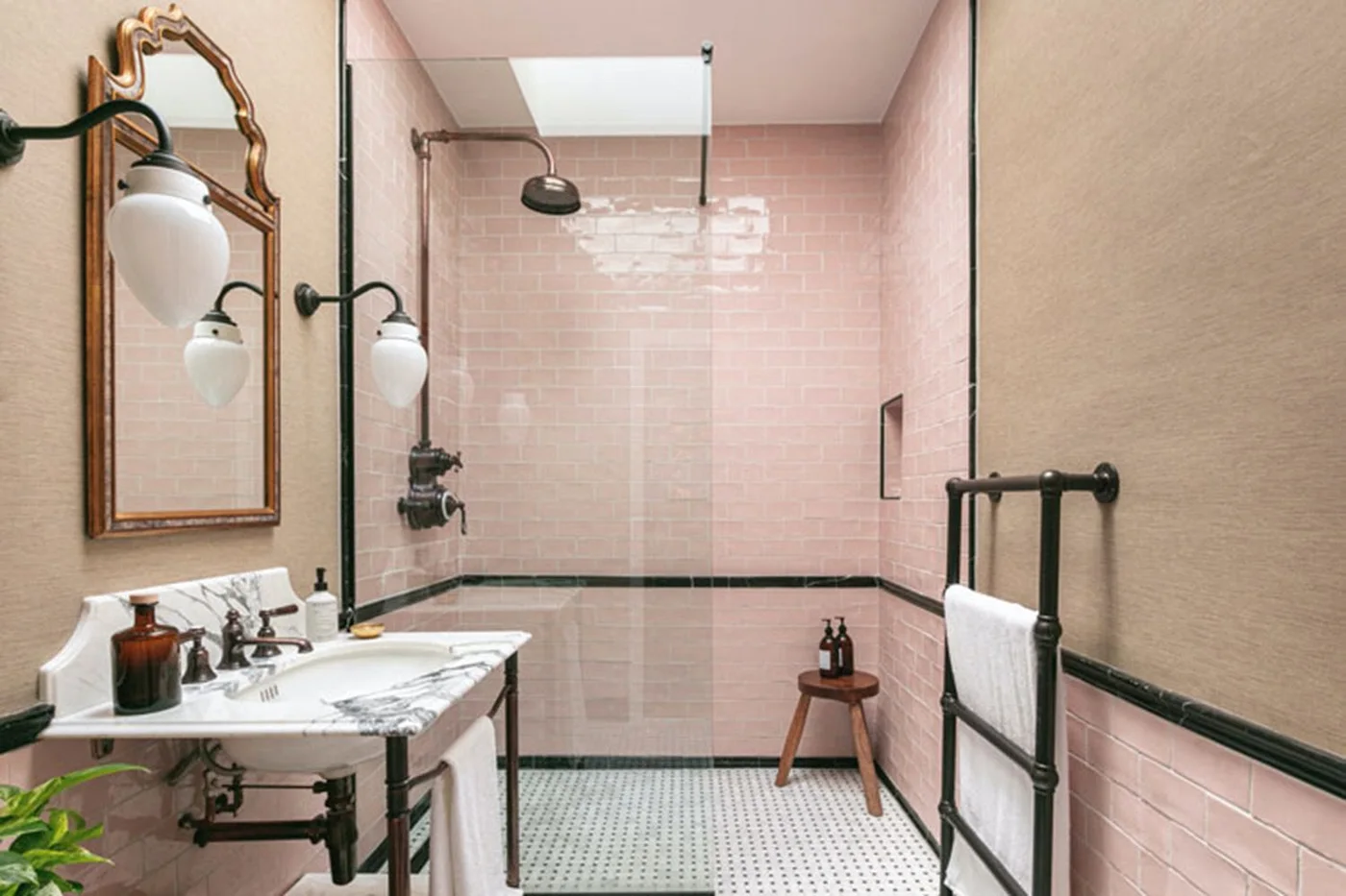 Glossy pale pink tiles line a shower beside dark border trim, a pale basin stand and dark fittings