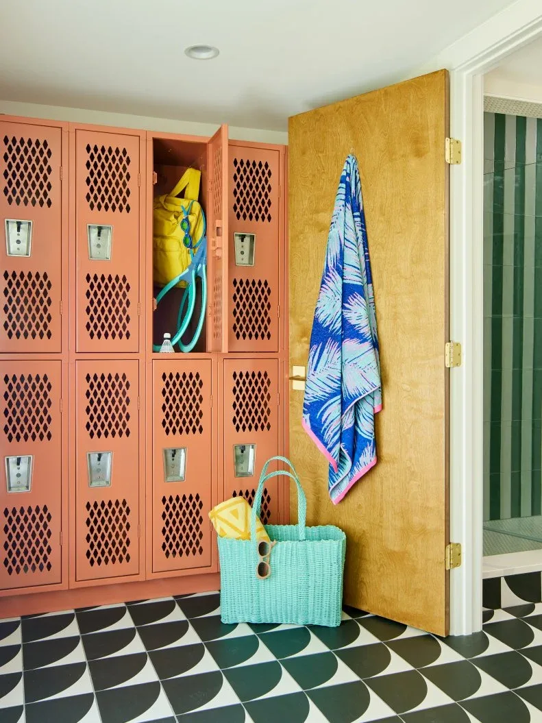 Mudroom with coral lockers, warm yellow door, blue patterned towel, turquoise bag and black and white patterned floor.