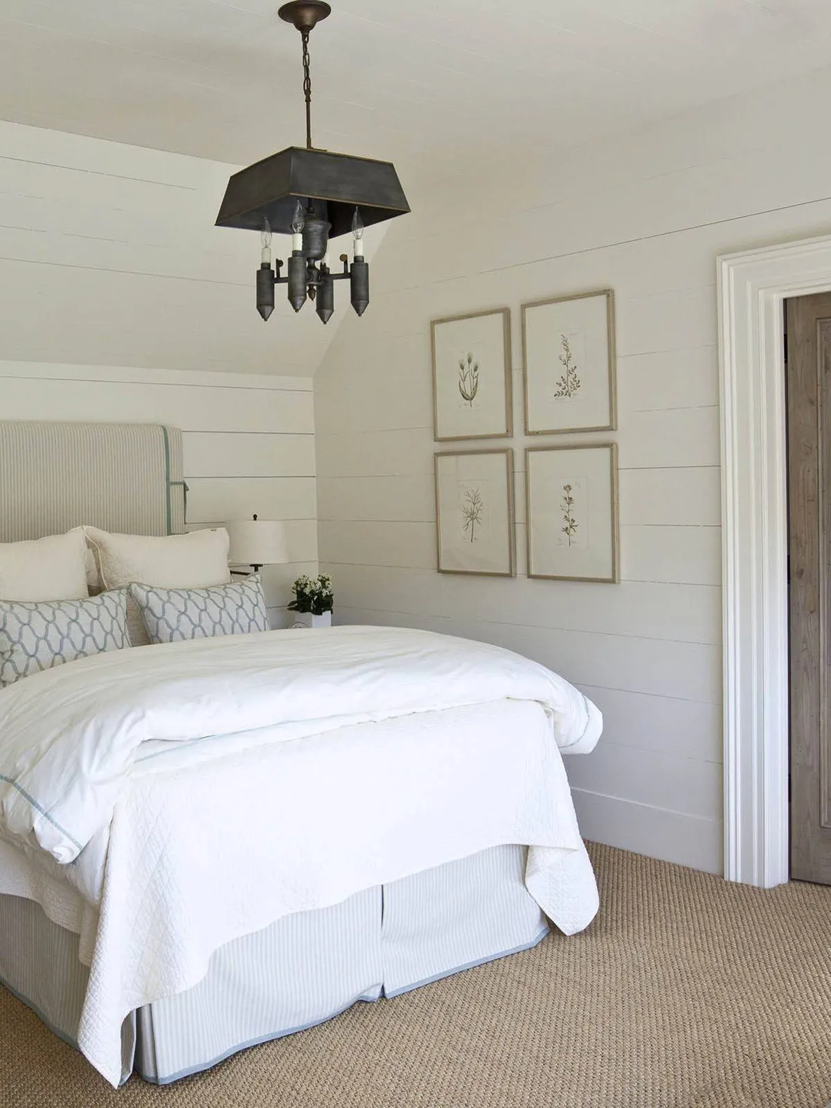 Four small framed pictures sit beside a white bed against pale walls.
