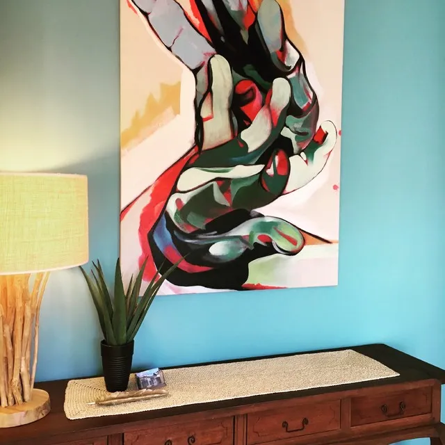 A colorful abstract picture hangs against a blue wall above a warm timber console.