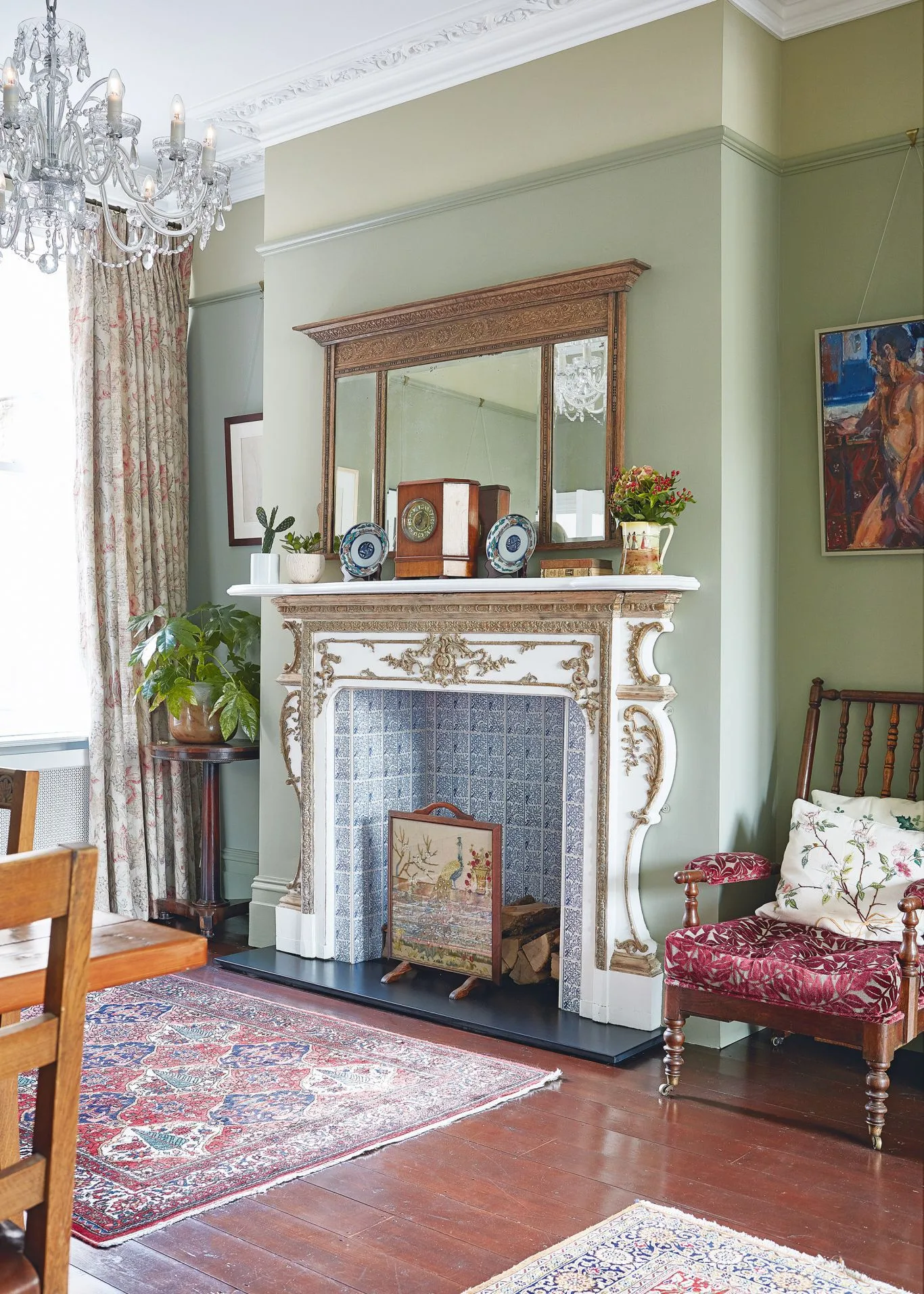 Ornate pale fireplace with blue tiled opening, small illustrated screen and patterned rugs