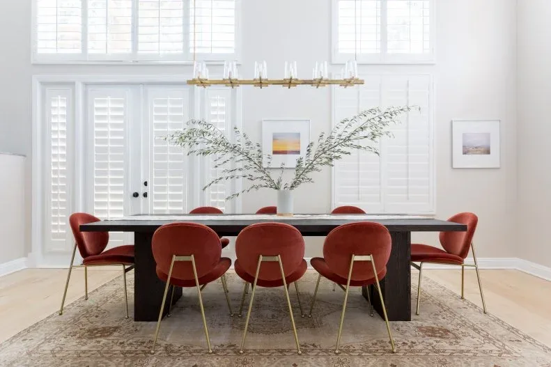 Coral rounded dining chairs with slim gold-toned legs around a dark rectangular table beneath a linear light.
