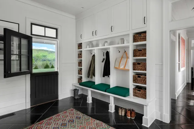 White entry storage surrounds a green bench cushion above dark flooring and a patterned rug.