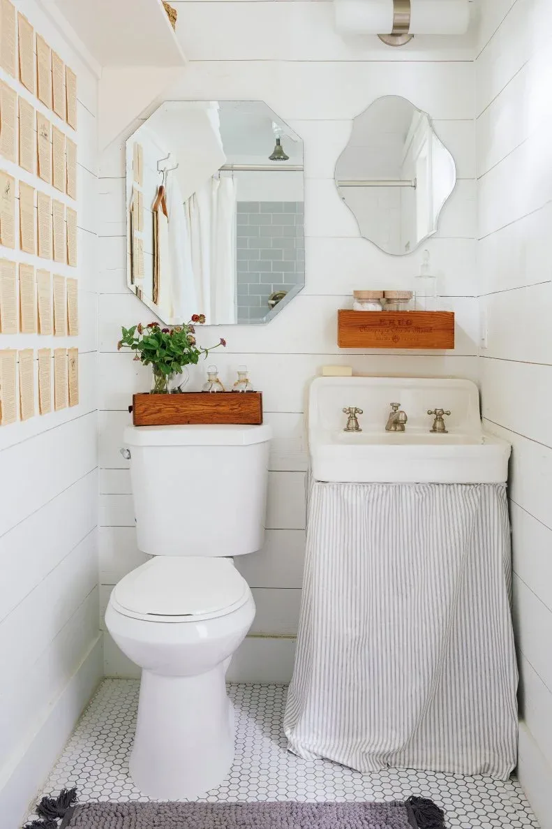 Narrow white paneled powder room with toilet, small basin and striped skirt, irregular mirrors and two wood wall boxes