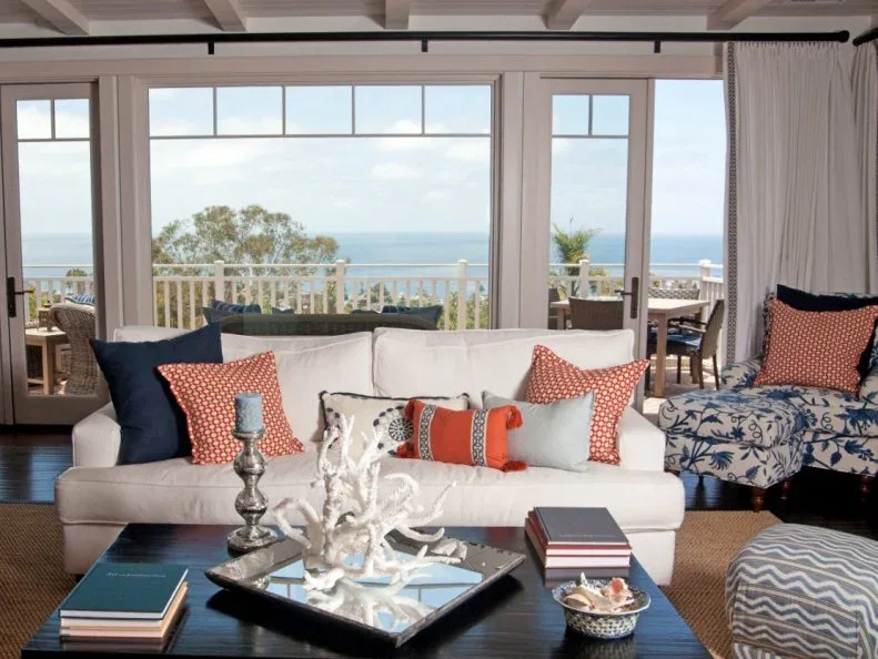 Pale sofa with red patterned cushions, a blue-and-white chair and dark coffee table beside sea-view doors.