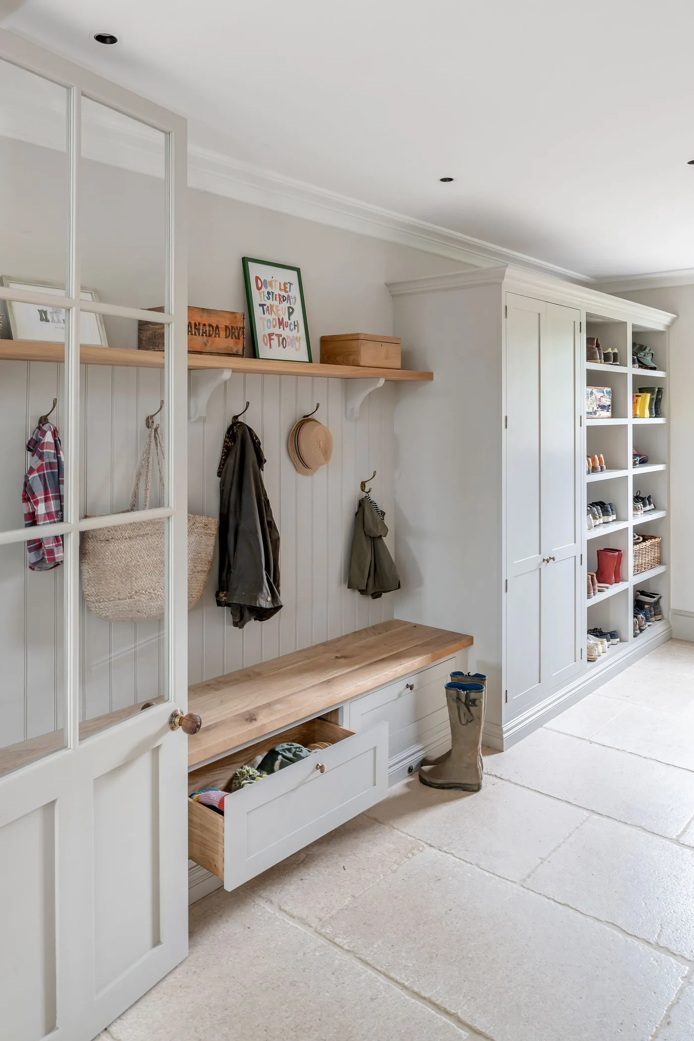 White entry storage with a wood bench, an open lower drawer, wall hooks, upper shelf and tall side cupboard